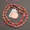 A strand of faceted strawberry quartz oval beads coiled around a penny for scale