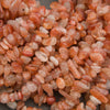 A pile of small peachy-pink polished gemstone beads with white inventory tags attached, photographed close-up on a gray surface.