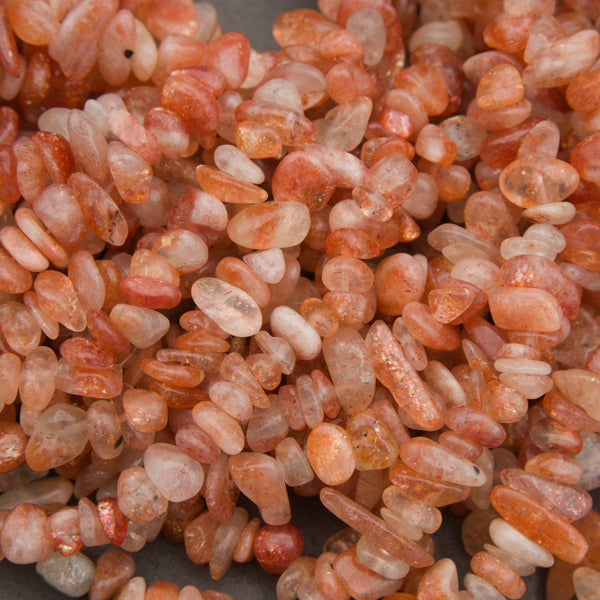 A pile of small peachy-pink polished gemstone beads with white inventory tags attached, photographed close-up on a gray surface.