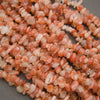 A pile of small peachy-pink polished gemstone beads with white inventory tags attached, photographed close-up on a gray surface.