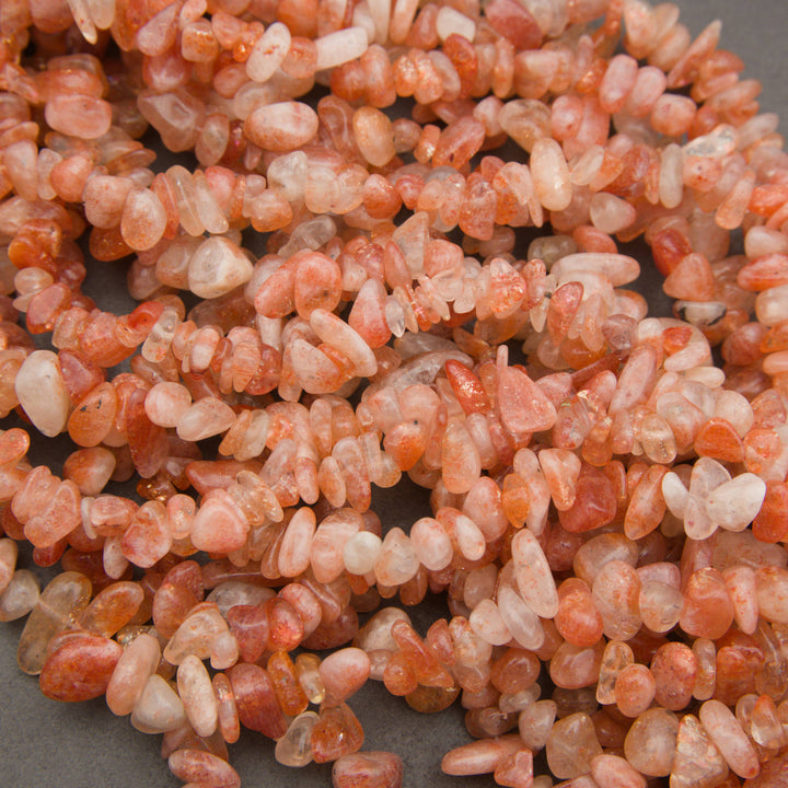 A pile of small peachy-pink polished gemstone beads with white inventory tags attached, photographed close-up on a gray surface.