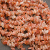 A pile of small peachy-pink polished gemstone beads with white inventory tags attached, photographed close-up on a gray surface.
