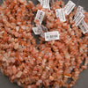 A pile of small peachy-pink polished gemstone beads with white inventory tags attached, photographed close-up on a gray surface.