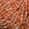 A close-up pile of polished peach-orange translucent gemstone beads with natural inclusions.