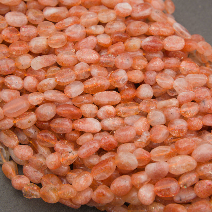 A close-up pile of peachy orange translucent oval beads with natural inclusions, set against a dark gray background.