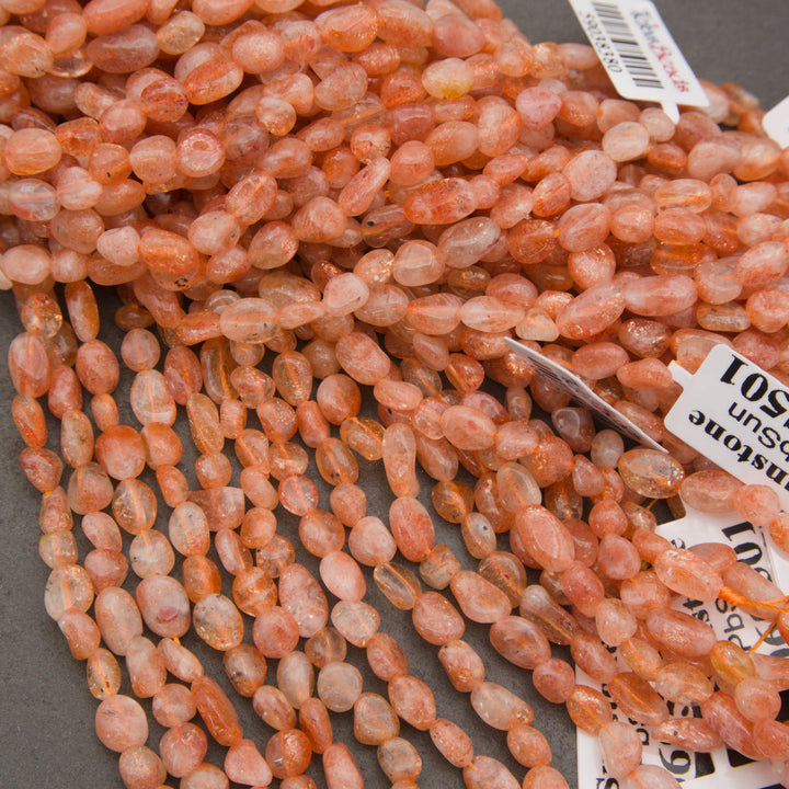 A close-up pile of peachy orange translucent oval beads with natural inclusions, set against a dark gray background.