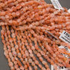 A close-up pile of peachy orange translucent oval beads with natural inclusions, set against a dark gray background.
