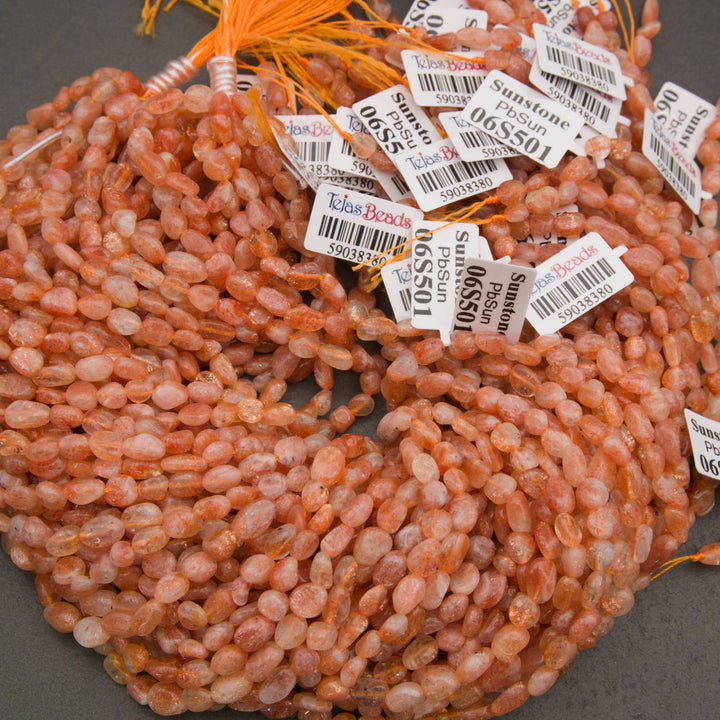 A close-up pile of peachy orange translucent oval beads with natural inclusions, set against a dark gray background.