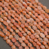 A close-up pile of peachy orange translucent oval beads with natural inclusions, set against a dark gray background.