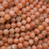 A close-up pile of polished round beads in a warm peachy orange color with natural marbling and translucent qualities.
