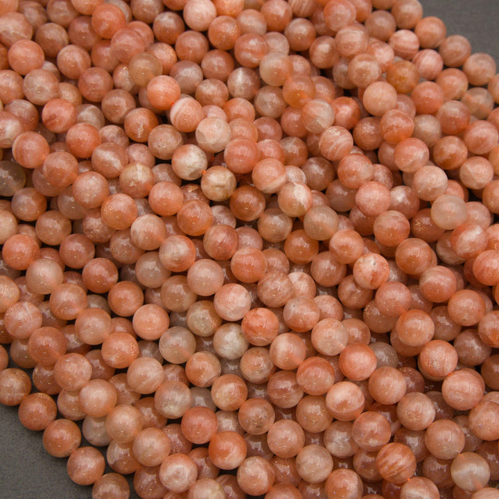 A close-up pile of polished round beads in a warm peachy orange color with natural marbling and translucent qualities.