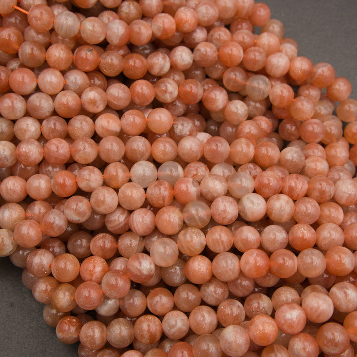 A close-up pile of round peach-pink stone beads with natural marbling and some translucent qualities.