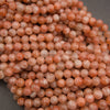 A close-up pile of round peach-pink stone beads with natural marbling and some translucent qualities.