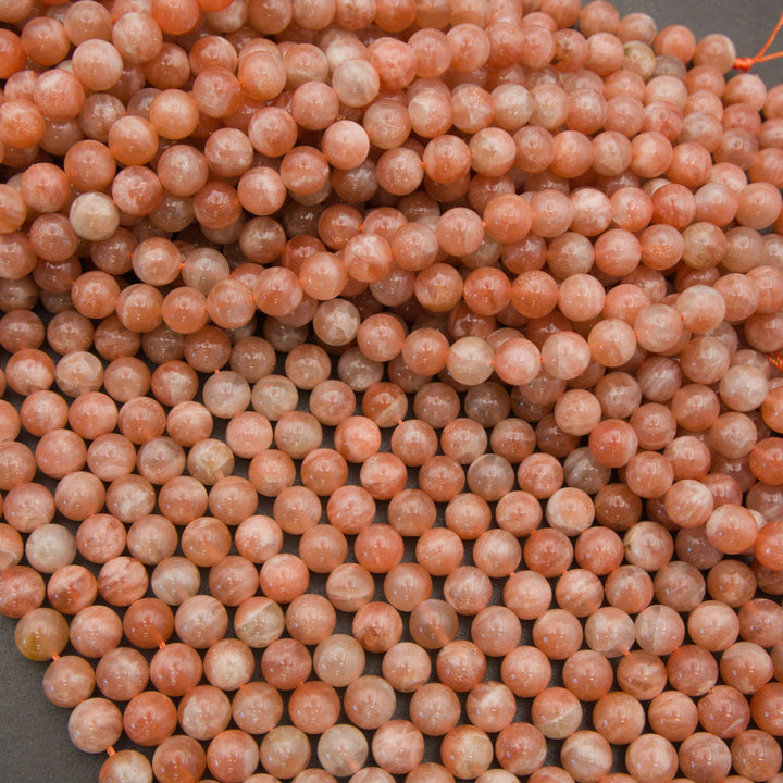 A close-up pile of round peach-pink stone beads with natural marbling and some translucent qualities.