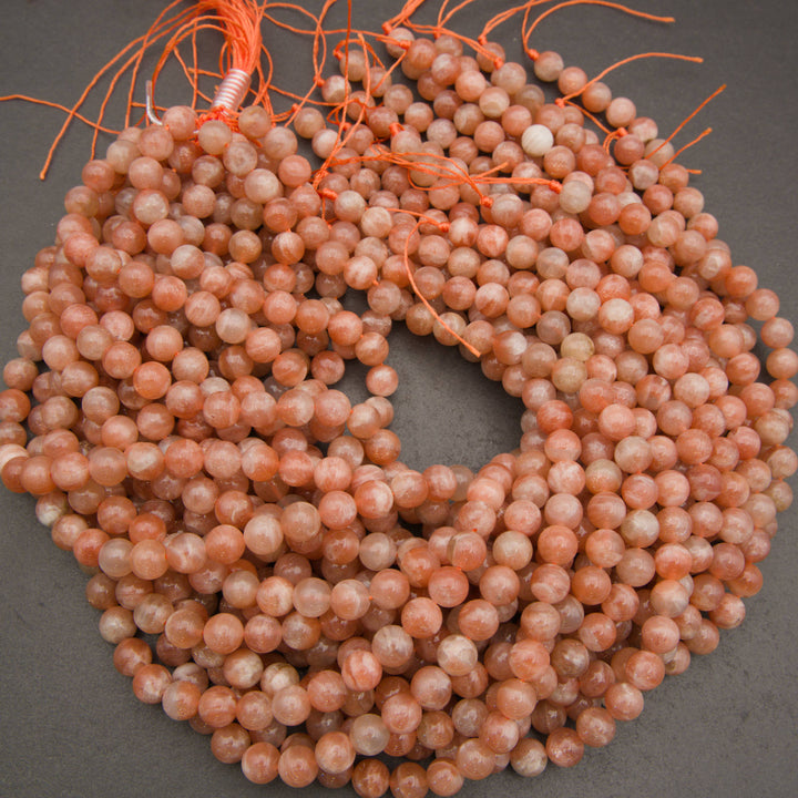 Multiple strands of round peach-orange stone beads with orange cord ties, arranged in a circle on a dark gray background.
