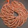 Multiple strands of round peach-orange stone beads with orange cord ties, arranged in a circle on a dark gray background.
