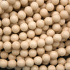 A dense pile of small, smooth, glossy round beads in a warm cream or light tan color, filling the entire frame.