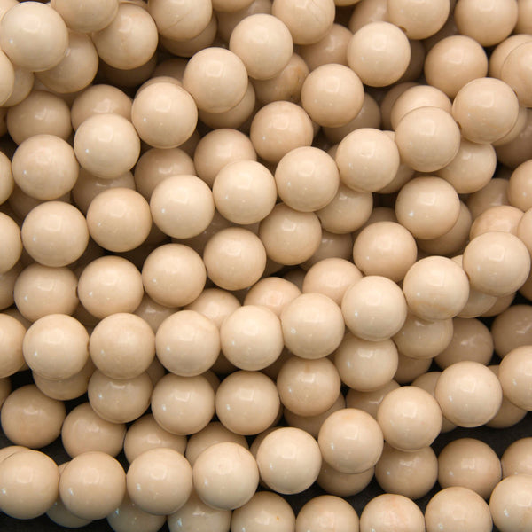 A dense pile of small, smooth, glossy round beads in a warm cream or light tan color, filling the entire frame.
