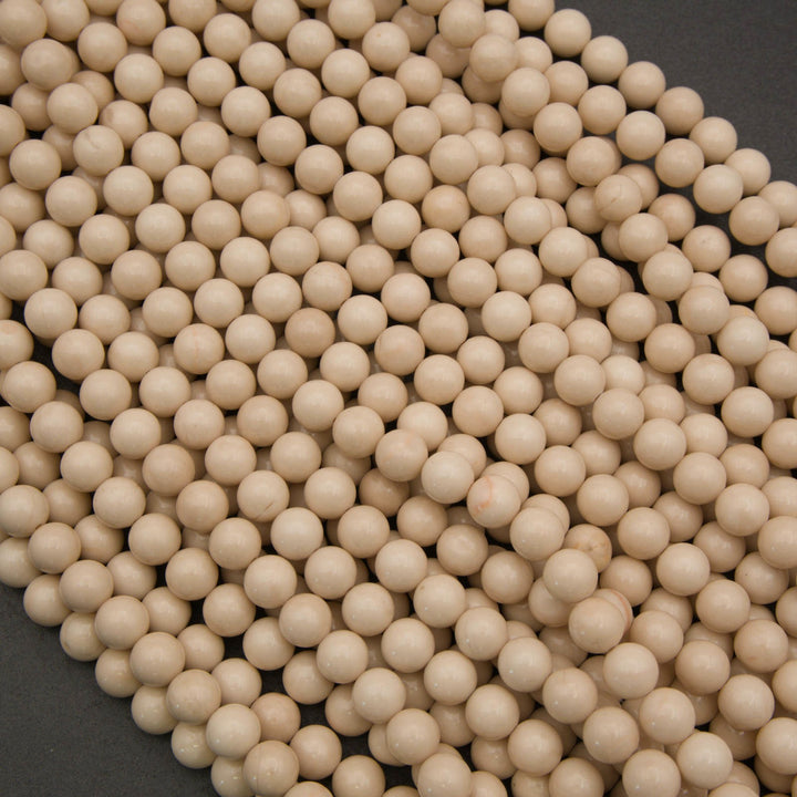A pile of small, smooth, light beige wooden beads on a dark gray background.