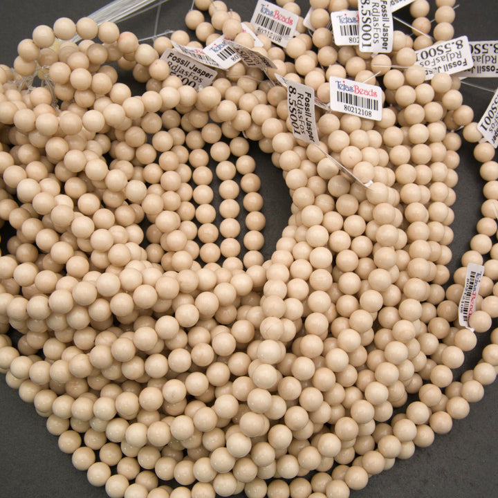 Multiple strands of small, round, light natural wood beads with attached white price tags, arranged on a dark gray surface.
