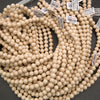 Multiple strands of small, round, light natural wood beads with attached white price tags, arranged on a dark gray surface.