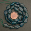 Blue beads arranged in a circular pattern with a penny for size comparison on a gray background