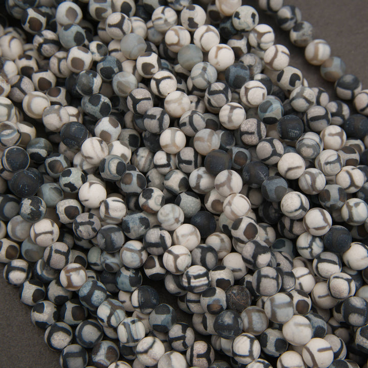 A pile of small round beads with a mottled black, white, and gray stone pattern, photographed close-up against a dark neutral background.