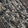 A pile of small round beads with a mottled black, white, and gray stone pattern, photographed close-up against a dark neutral background.