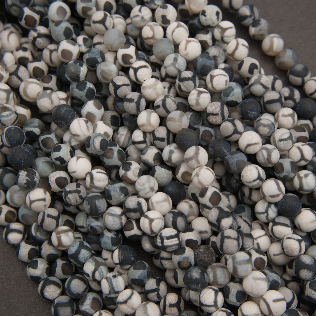 A pile of small round beads with a mottled black, white, and gray stone pattern, photographed close-up against a dark neutral background.