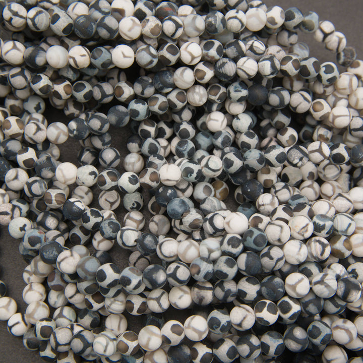 A close-up pile of small round beads with a black and white mottled, speckled pattern.