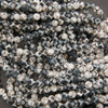 A close-up pile of small round beads with a black and white mottled, speckled pattern.
