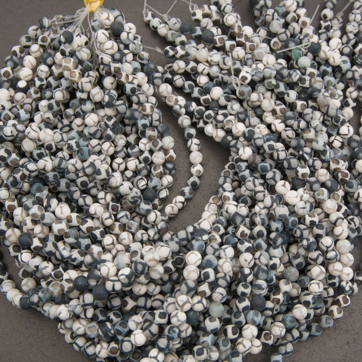 Multiple strands of faceted gemstone beads in a mottled pattern of white, gray, and dark blue-gray, arranged on a dark gray surface.
