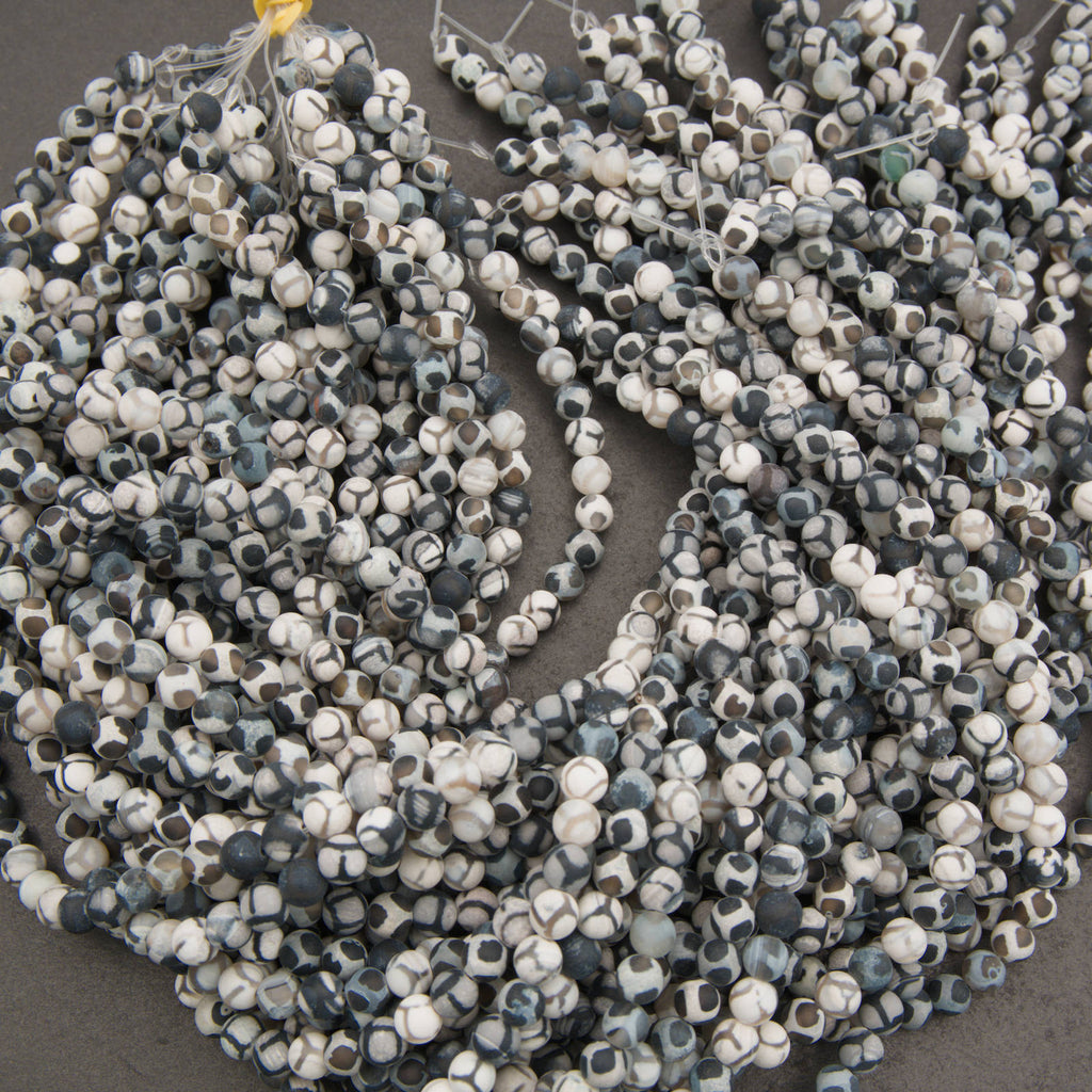 Multiple strands of faceted gemstone beads in a mottled pattern of white, gray, and dark blue-gray, arranged on a dark gray surface.