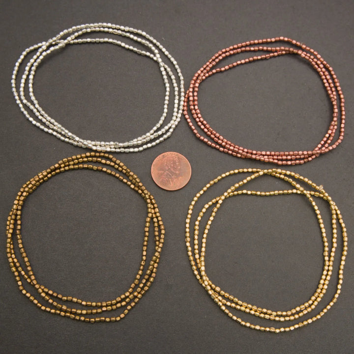 Four sets of beaded necklaces in silver, copper, and gold on a dark surface with a penny for scale.