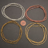 Four sets of beaded necklaces in silver, copper, and gold on a dark surface with a penny for scale.