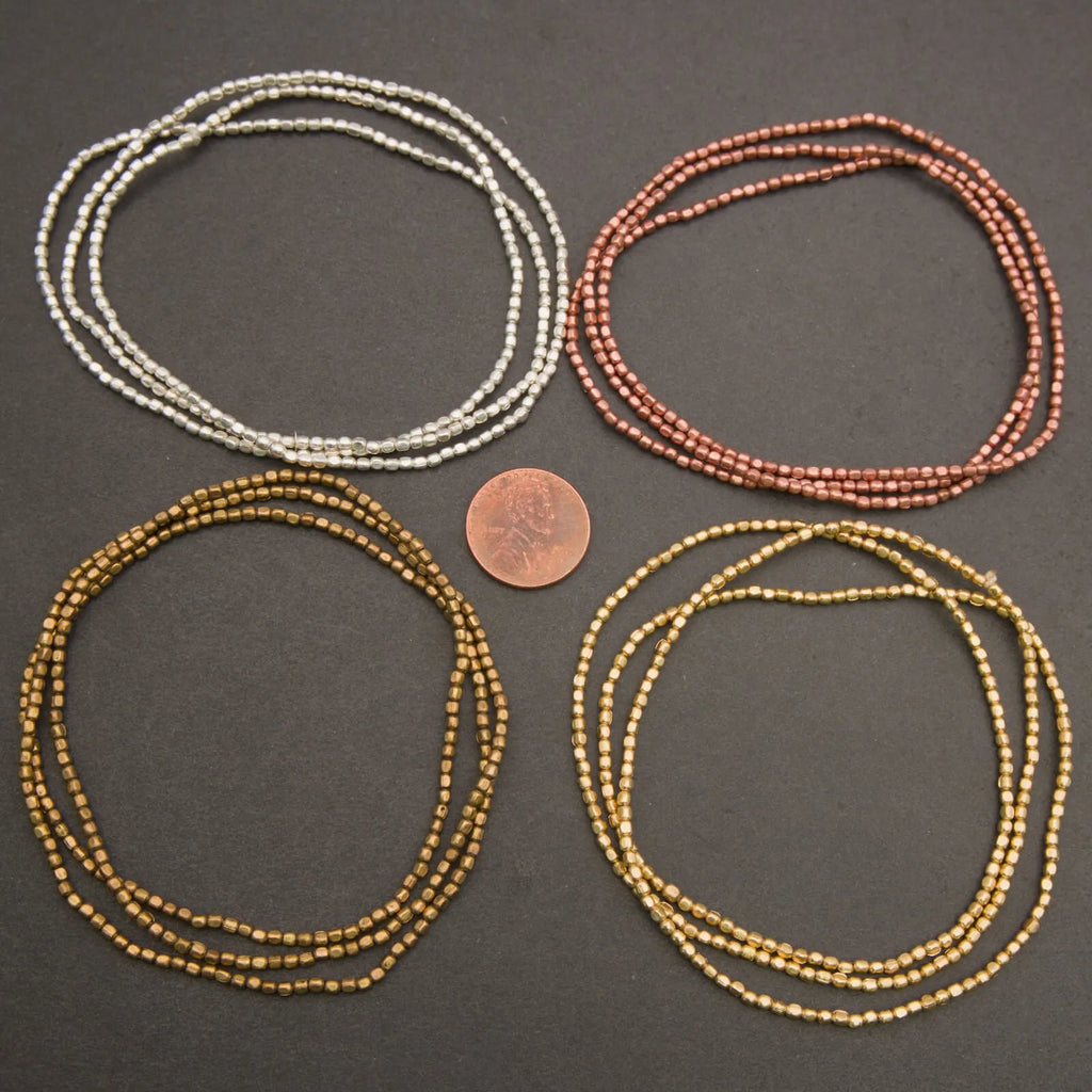 Four sets of beaded necklaces in silver, copper, and gold on a dark surface with a penny for scale.