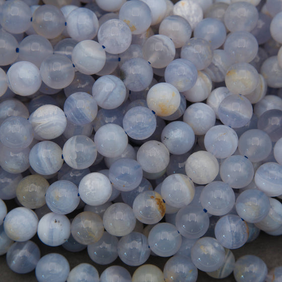 A pile of round, translucent pale blue and white beads with natural stone inclusions, arranged on a neutral gray surface.