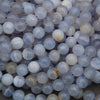 A pile of round, translucent pale blue and white beads with natural stone inclusions, arranged on a neutral gray surface.