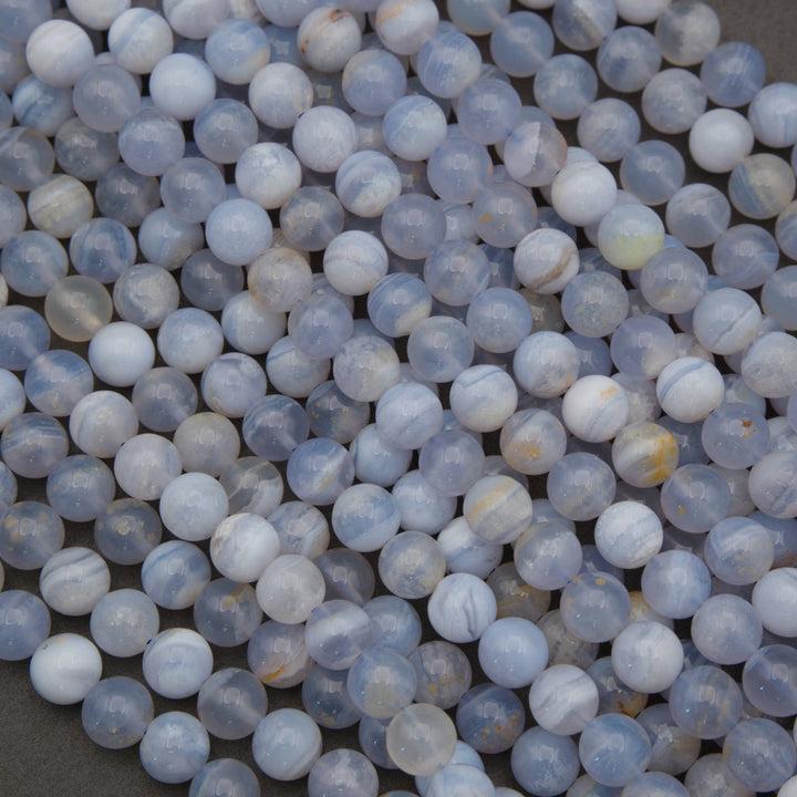 A pile of small round translucent beads in pale blue, white, and gray with some faint yellowish veining, photographed close up on a neutral surface.