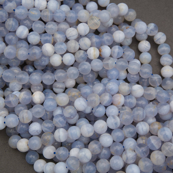 A pile of round, translucent pale blue and white beads with natural stone inclusions, arranged on a neutral gray surface.