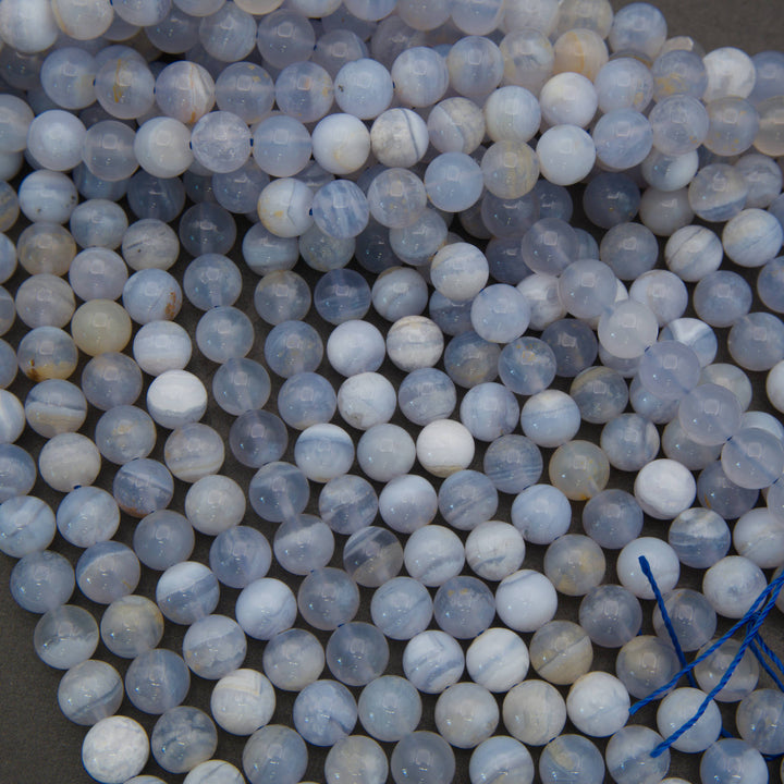 A pile of round, polished gemstone beads in pale blue, white, and gray with subtle banding, strung together with a blue cord.