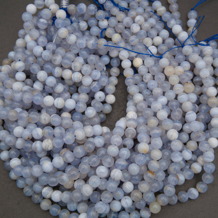 A pile of round, pale blue and white marbled gemstone beads strung on blue thread, photographed close-up against a neutral gray background.