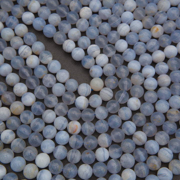 A close-up of many small round beads or cabochons in pale blue, white, and gray with some faint marbling, filling the frame on a dark surface.