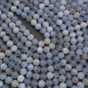 A close-up of many small round beads or cabochons in pale blue, white, and gray with some faint marbling, filling the frame on a dark surface.