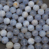 A close-up pile of round, polished gemstone beads in pale blue, white, and gray with subtle marbled patterns and a few small warm yellowish inclusions.