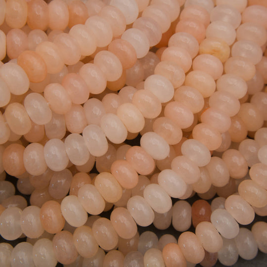 Close-up of multiple strands of smooth, oval beads in soft peach, cream, and pale pink tones.