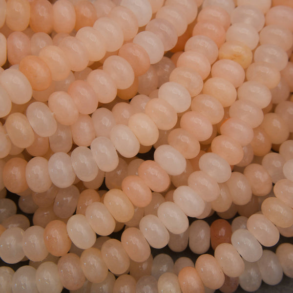 Close-up of multiple strands of smooth, oval beads in soft peach, cream, and pale pink tones.