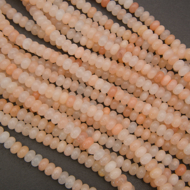Multiple strands of small faceted round beads in a soft peach, cream, and pale pink stone, arranged diagonally on a dark gray background.