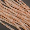 Multiple strands of small faceted round beads in a soft peach, cream, and pale pink stone, arranged diagonally on a dark gray background.