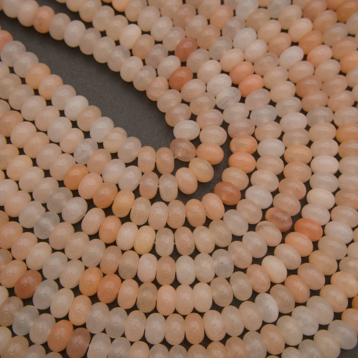 Close-up of multiple strands of small oval beads in soft peach, cream, and light tan tones arranged on a dark gray surface.